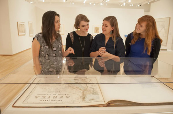 Figure 5. Student curators (left to right) Rachel Fleder, Lauren Jackson, Elizabeth Blackwood, and Jordan Noyes discuss Hermann Habenicht’s Spezial-Karte von Afrika (1887) in the exhibition space for “Defining Lines: Cartography in the Age of Empire.”