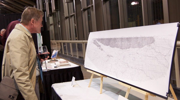 A conference attendee looking at a black-and-white map entitled The Western Shore of Lake Michigan. The map, several feet wide, is sitting on a stand that is atop a table. Photo by Dylan Moriarty.