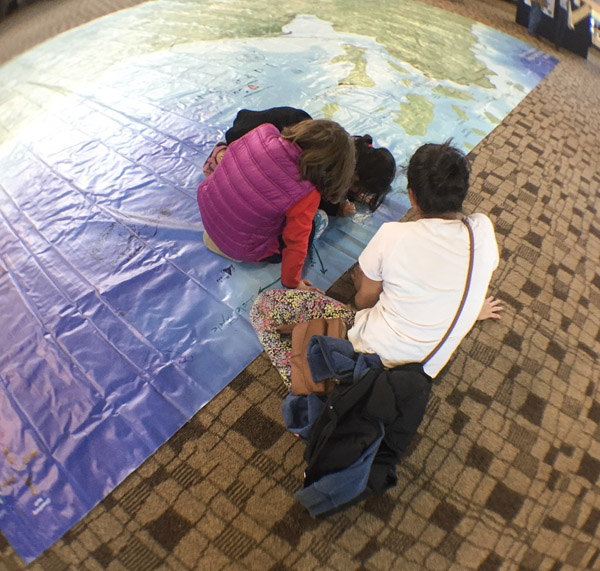 Several people seated on top of or next to a large map on the floor. The map is the size of a small billboard and glossy. It depicts lands and waters in northern Wisconsin. Photo by Matt Dooley.