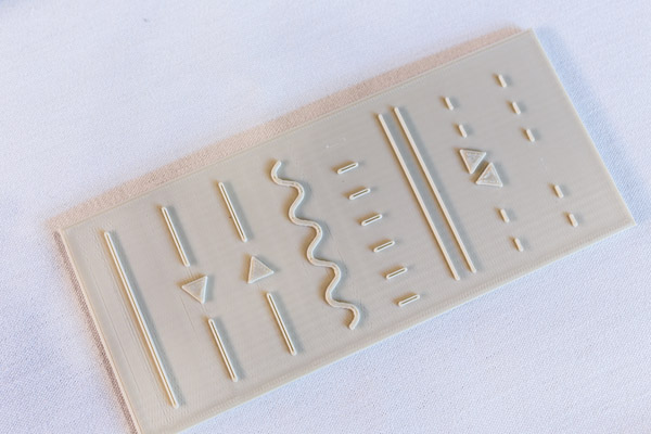 A small, off-white block with raised relief. The relief is shaped to show various cartographic line patterns, triangles, and dashes. Photo by Charles P. Rader.