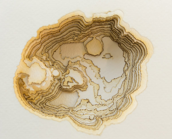 A close-in view of another sculpture of Crater Lake, formed from stacked sheets of paper which have each had holes cut in them. The edges of each cut area appear brown and singed. The pages are not painted, but remain the natural color of the paper. Photo by Charles P. Rader