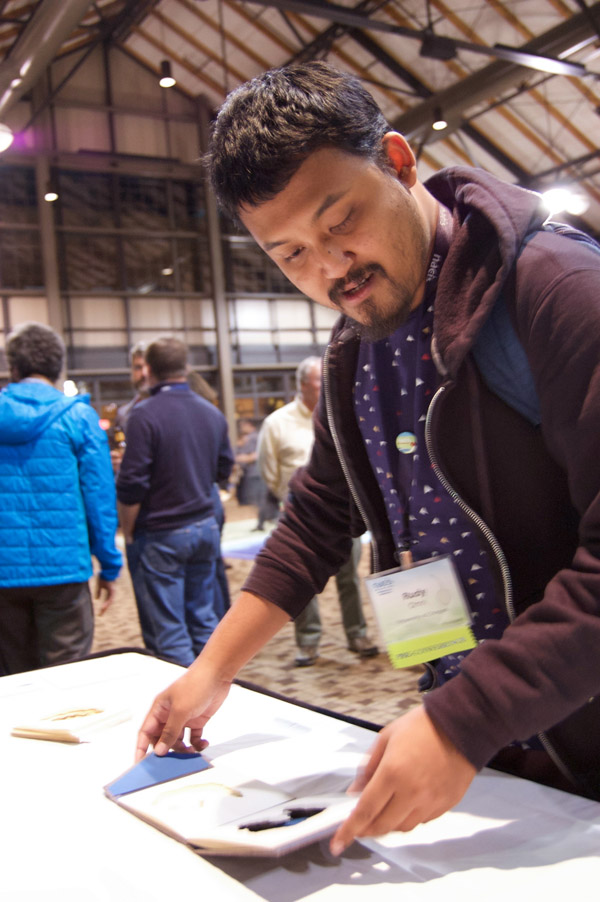 A person holding and looking at one of the small book sculptures, which is sitting on a table in a large, crowded room. Photo by Dylan Moriarty