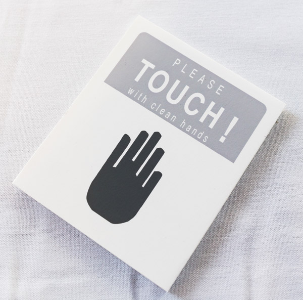 A sign labeled 'Please Touch! With clean hands' The paper is white, as is the text, which is on a grey background. Below the text is a large icon of a hand, in black. Photo by Charles P. Rader